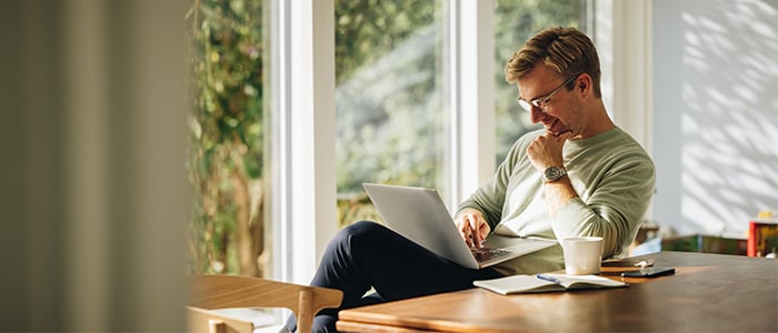 Adult working at home on a laptop with some paperwork next to them