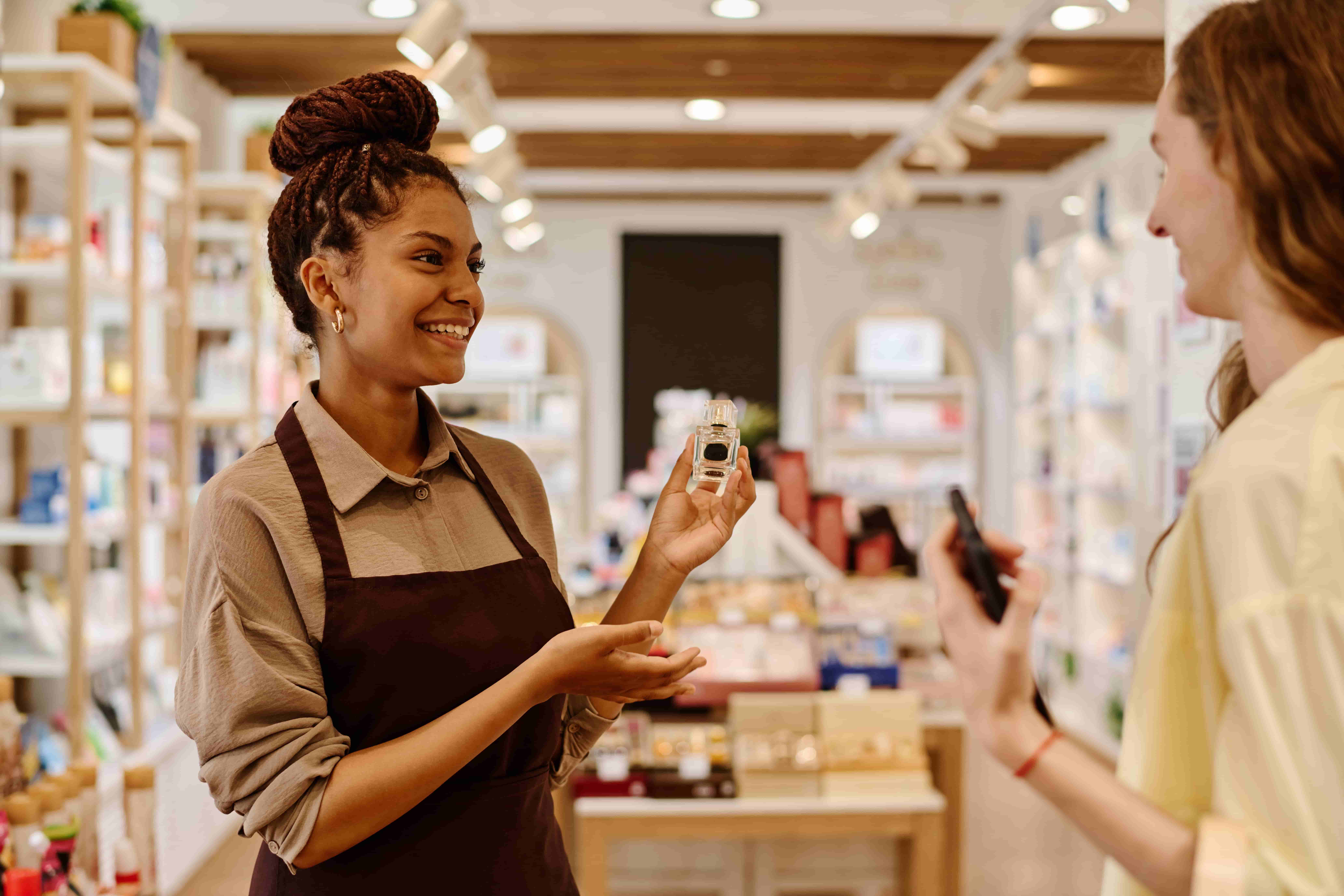 A sales representative in a beauty store offering a customer a perfume to try