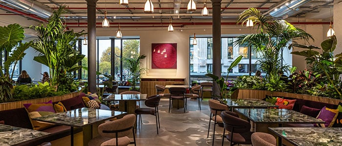 a vibrant Louis Vuitton café featuring numerous tables surrounded by lush greenery and decorative plants